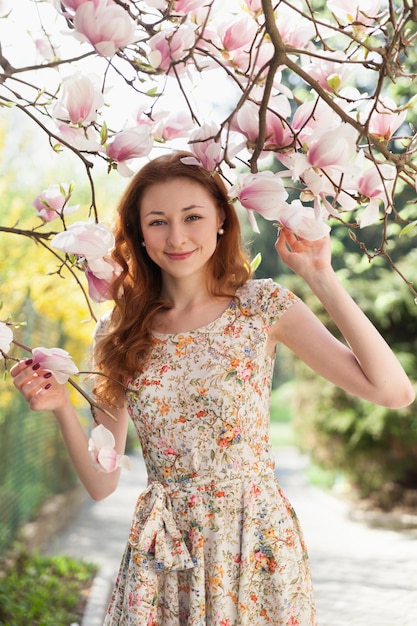 Jonge gemberhaarvrouw dichtbij lichtroze tedere tot bloei komende boom. fee dromerige sfeer van de lente en de zomer. Mooie romantische dame lachende bruid, bruiloft. Kopieer ruimte achtergrond.