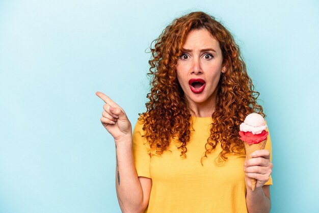 Jonge gembervrouw met een ijsje geïsoleerd op een blauwe achtergrond die naar de zijkant wijst