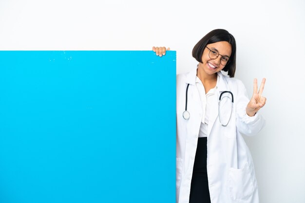 Jonge gemengd ras arts vrouw met een groot bord geïsoleerd glimlachend en overwinningsteken tonen