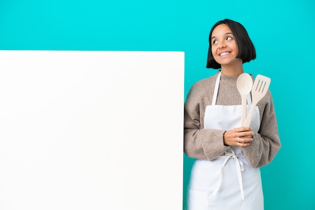 Jonge gemengd ras kok vrouw met een groot bord geïsoleerd op blauwe achtergrond een idee denken tijdens het opzoeken