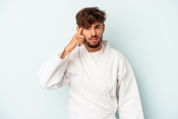 Jonge gemengd ras man doet karate geïsoleerd op blauwe achtergrond met een gebaar van teleurstelling met wijsvinger.