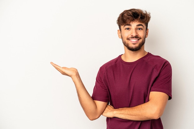 Jonge gemengd ras man geïsoleerd op een grijze achtergrond met een kopie ruimte op een palm en met een andere hand op de taille.