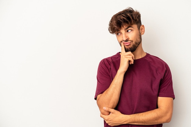 Jonge gemengd ras man geïsoleerd op een grijze achtergrond op zoek zijwaarts met twijfelachtige en sceptische uitdrukking.