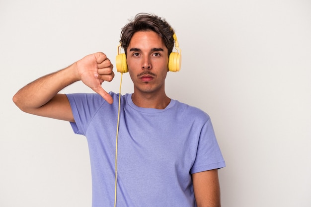 Jonge gemengd ras man luisteren naar muziek geïsoleerd op blauwe achtergrond met een afkeer gebaar, duim omlaag. Onenigheid begrip.