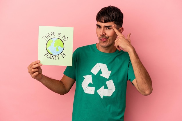 Jonge gemengd ras man met een er is geen planeet b plakkaat geïsoleerd op roze achtergrond