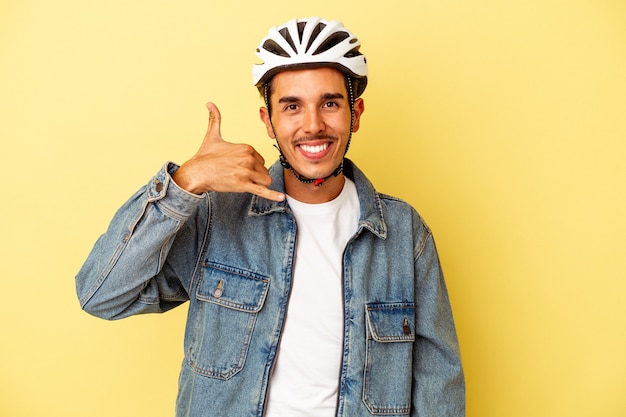 Jonge gemengd ras man met een helm fiets geïsoleerd op een gele achtergrond met een mobiel telefoongesprek gebaar met vingers.