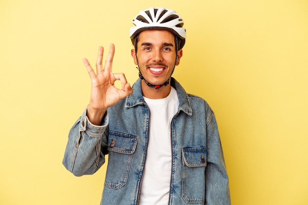 Jonge gemengd ras man met een helm fiets geïsoleerd op gele achtergrond vrolijk en zelfverzekerd weergegeven: ok gebaar.