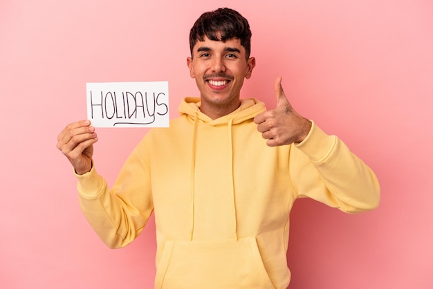 Foto jonge gemengd ras man met een vakantie plakkaat geïsoleerd op roze achtergrond