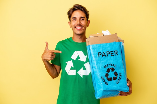 Jonge gemengd ras man recycling papier geïsoleerd op gele achtergrond persoon met de hand wijzend naar een shirt kopie ruimte, trots en zelfverzekerd