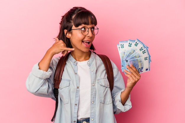 Jonge gemengd ras student vrouw met rekeningen geïsoleerd op roze achtergrond met een mobiel telefoongesprek gebaar met vingers.