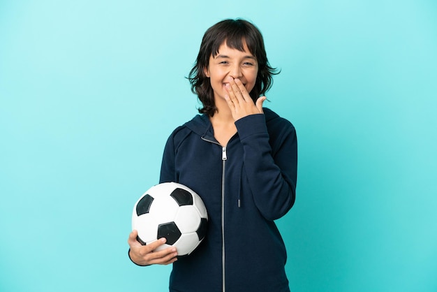 Jonge gemengd ras voetballer vrouw geïsoleerd op blauwe achtergrond gelukkig en lachend die mond bedekken met hand
