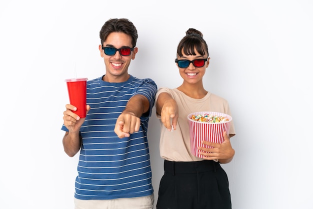 Jonge gemengd ras vrienden geïsoleerd op een witte achtergrond met 3d-bril en houden een grote emmer popcorns terwijl ze naar voren wijzen