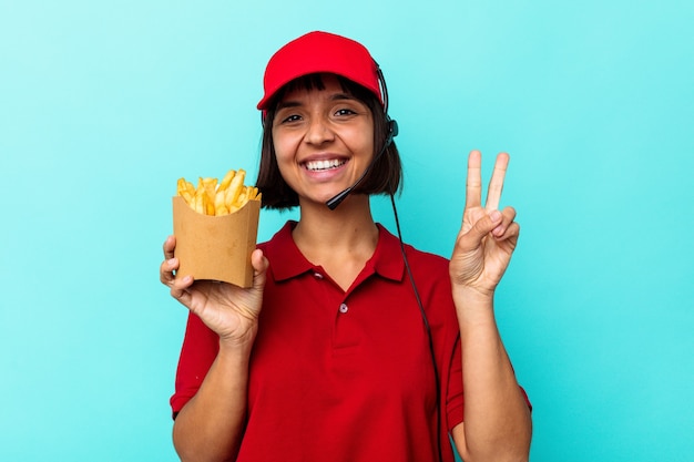 Jonge gemengd ras vrouw fastfood restaurant werknemer met frietjes geïsoleerd op blauwe achtergrond met nummer twee met vingers.