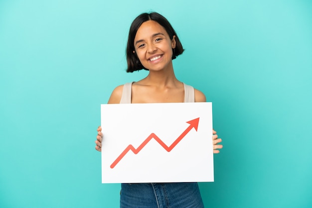 Jonge gemengd ras vrouw geïsoleerd op blauwe achtergrond met een bord met een groeiend statistiek pijlsymbool met gelukkige uitdrukking