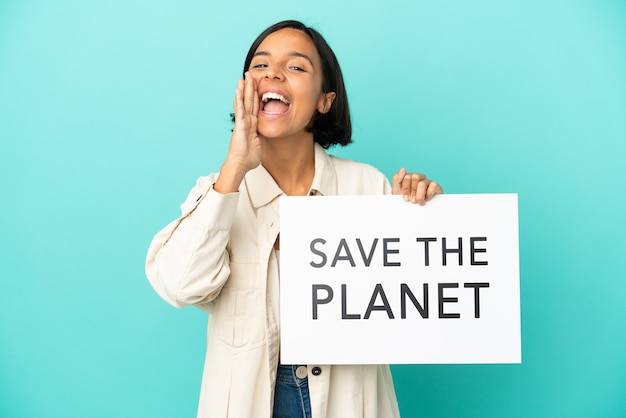 Jonge gemengd ras vrouw geïsoleerd op blauwe achtergrond met een bordje met de tekst Save the Planet en schreeuwen shout