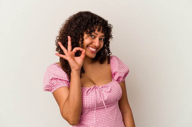 Jonge gemengd ras vrouw geïsoleerd op een witte achtergrond knipoogt een oog en houdt een goed gebaar met de hand.