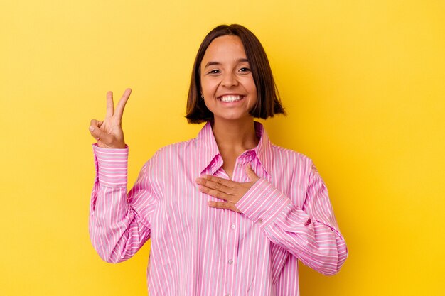 Jonge gemengd ras vrouw geïsoleerd op gele achtergrond een eed afleggen, hand op de borst zetten.