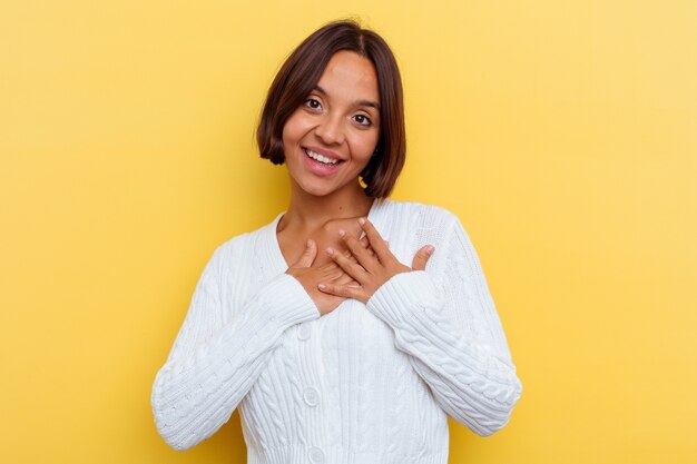 Jonge gemengd ras vrouw geïsoleerd op gele achtergrond heeft vriendelijke uitdrukking, handpalm tegen borst te drukken. Liefde concept.