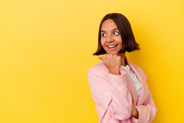 Jonge gemengd ras vrouw geïsoleerd op gele achtergrond punten met duim vinger weg, lachen en zorgeloos.