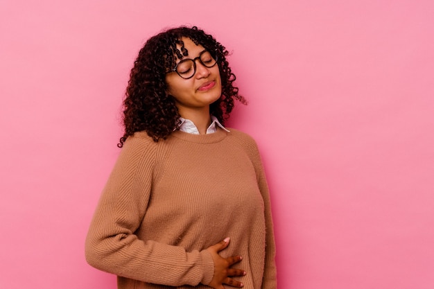 Jonge gemengd ras vrouw geïsoleerd op roze achtergrond raakt buik, glimlacht zachtjes, eten en tevredenheid concept.