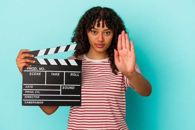 Jonge gemengd ras vrouw met een Filmklapper geïsoleerd op blauwe achtergrond staande met uitgestrekte hand weergegeven: stopbord, voorkomen dat u.