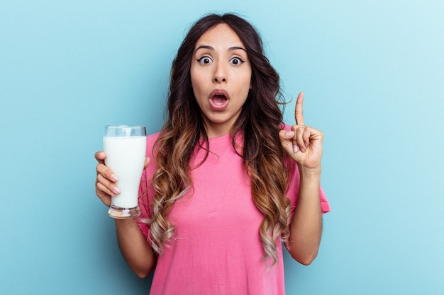 Jonge gemengd ras vrouw met een glas melk geïsoleerd op blauwe achtergrond met een idee, inspiratie concept.