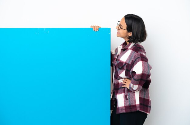 Jonge gemengd ras vrouw met een groot blauw bordje geïsoleerd op een witte achtergrond in laterale positie