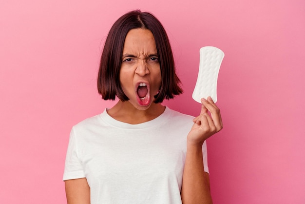 Jonge gemengd ras vrouw met een kompres geïsoleerd op roze achtergrond schreeuwen erg boos en agressief.