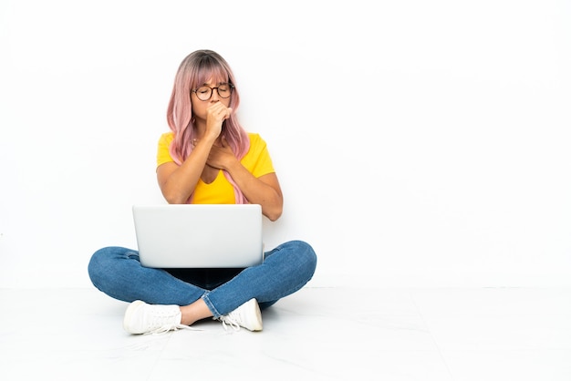 Jonge gemengd ras vrouw met een laptop met roze haar zittend op de vloer geïsoleerd op een witte achtergrond lijdt aan hoest en voelt zich slecht