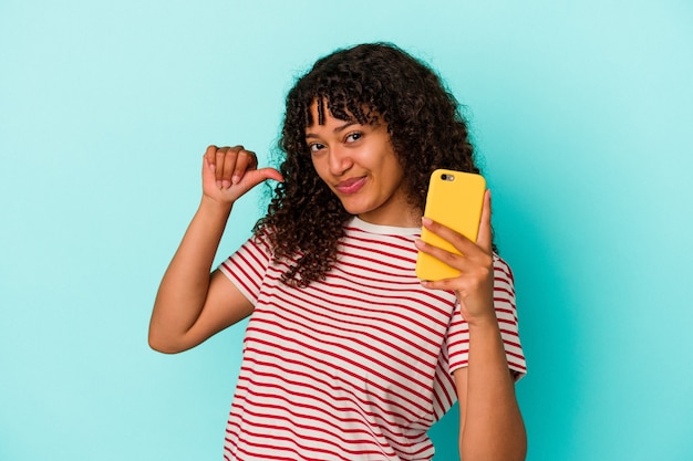 Jonge gemengd ras vrouw met een mobiele telefoon geïsoleerd op blauwe achtergrond voelt trots en zelfverzekerd, voorbeeld te volgen.