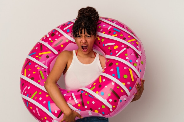 Jonge gemengd ras vrouw met een opblaasbare lucht donut geïsoleerd op een witte achtergrond schreeuwen erg boos en agressief.