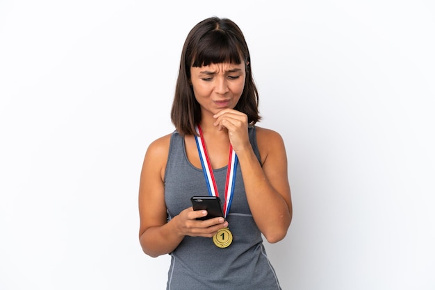Jonge gemengd ras vrouw met medailles geïsoleerd op een witte achtergrond denken en het verzenden van een bericht