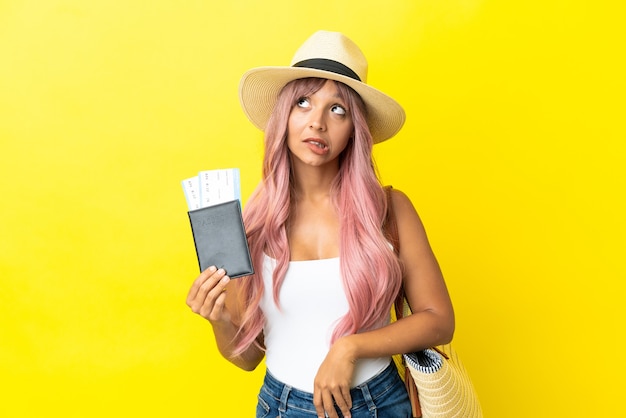 Jonge gemengd ras vrouw met paspoort en strandtas geïsoleerd op gele achtergrond en opzoeken