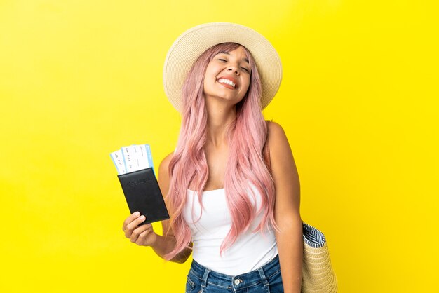 Jonge gemengd ras vrouw met paspoort en strandtas geïsoleerd op gele achtergrond lachen