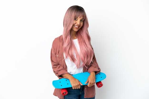 Jonge gemengd ras vrouw met roze haren geïsoleerd op een witte achtergrond met een skate met gelukkige expression