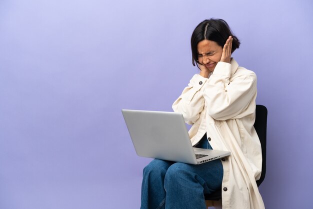 Jonge gemengd ras vrouw zittend op een stoel met laptop geïsoleerd op paarse achtergrond gefrustreerd en die oren bedekt