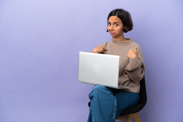 Jonge gemengd ras vrouw zittend op een stoel met laptop geïsoleerd op paarse achtergrond wijzend naar zichzelf one