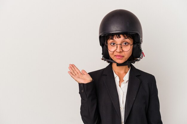 Jonge gemengd ras zakenvrouw draagt een motorhelm geïsoleerd met een kopie ruimte op een handpalm en houdt een andere hand op de taille.