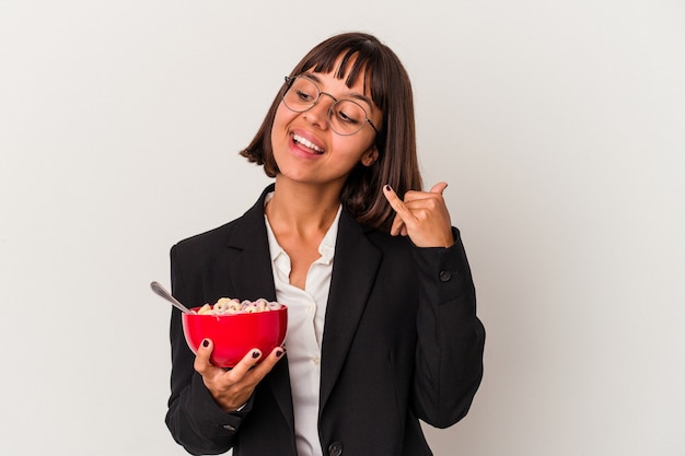 Jonge gemengd ras zakenvrouw eten granen geïsoleerd op een witte achtergrond met een mobiel telefoongesprek gebaar met vingers.