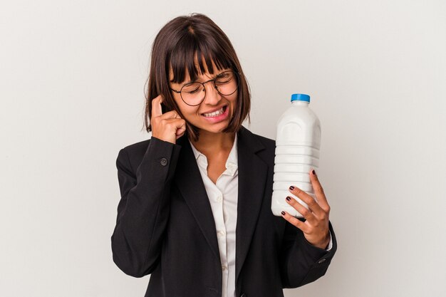 Jonge gemengd ras zakenvrouw met een melkfles geïsoleerd op een witte achtergrond die oren bedekt met handen.