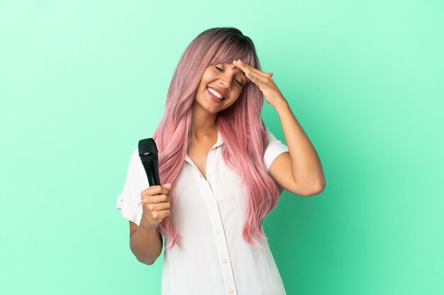 Jonge gemengd ras zanger vrouw met roze haren geïsoleerd op een groene achtergrond lacht veel