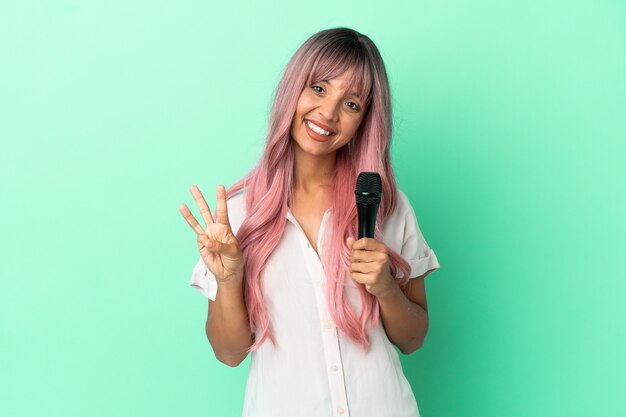 Jonge gemengd ras zanger vrouw met roze haren geïsoleerd op groene achtergrond gelukkig en drie tellen met vingers