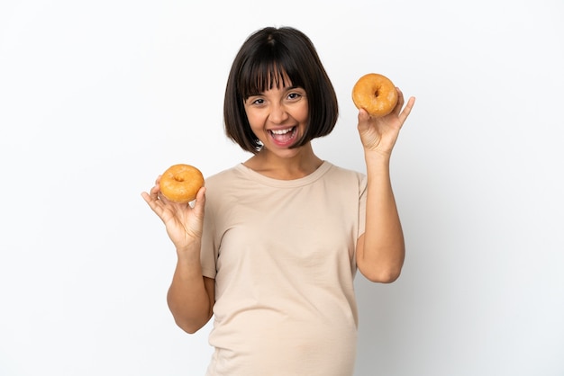 Jonge gemengd ras zwangere vrouw geïsoleerd op een witte achtergrond met donuts met gelukkige expression