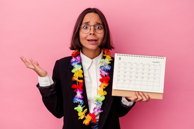 Jonge gemengde ras bedrijfsvrouw die de dagen telt voor vakanties die op roze verrast en geschokt muur worden geïsoleerd