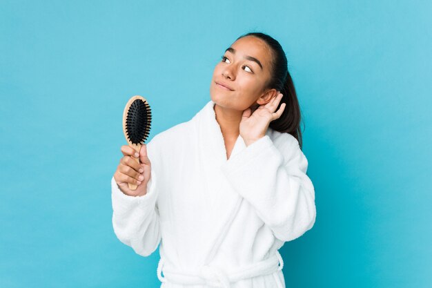 Jonge gemengde ras indiër die een haarborstel houdt die aan het luisteren van een roddel probeert.