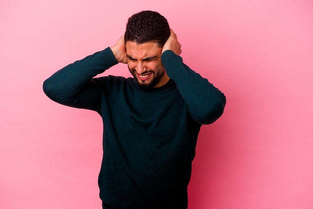 Jonge gemengde rasmens die op roze muur wordt geïsoleerd die oren met handen behandelt.