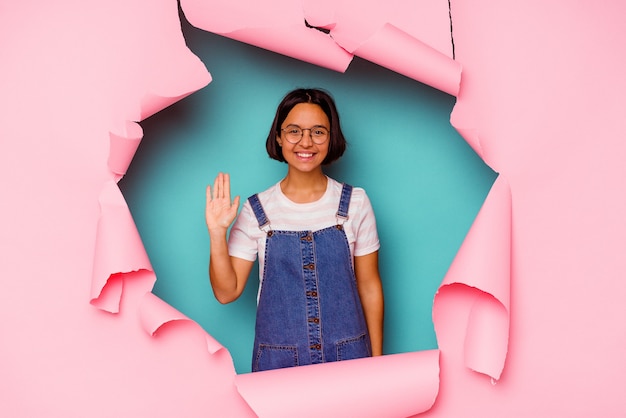 Jonge gemengde rasvrouw achter een gebroken achtergrond die gelukkig en zelfverzekerd glimlachen, kin met hand aanraken.