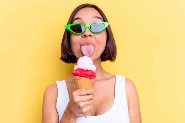 Jonge gemengde rasvrouw die een roomijs houdt dat op gele achtergrond wordt geïsoleerd