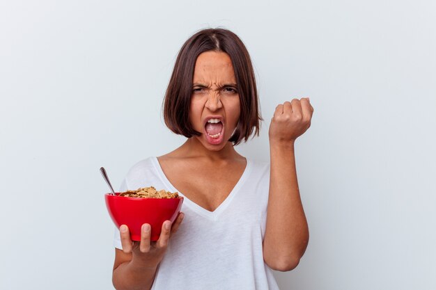 Jonge gemengde rasvrouw die granen eten die op witte achtergrond worden geïsoleerd die vuist verhogen na een overwinning, winnaarconcept.