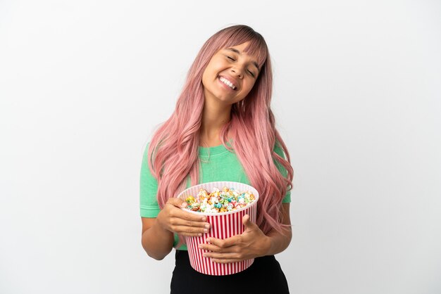 Jonge gemengde rasvrouw die met roze haar popcorn eet die op witte achtergrond wordt geïsoleerd